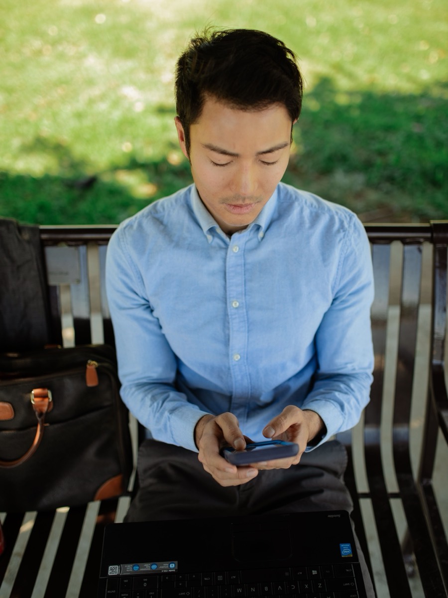 A student on a park bench running a station on their phone.